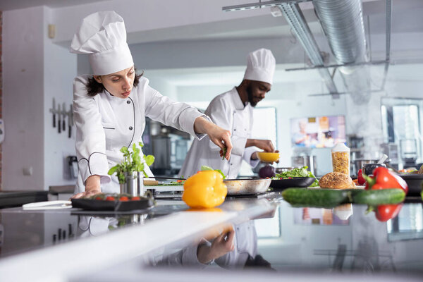 Female expert cook sprinkling tasty herbs to dish on the stove in kitchen, using fresh rosemary and spices to enhance the flavors and deliciousness while cooking the dish. Culinary arts.
