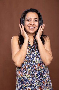 Kablosuz kulaklık takan neşeli genç Hintli kadın en sevdiği müziğin keyfini çıkarırken dans ediyor ve gülümsüyor. Stüdyoda kulaklığını tutan güzel bir kadın model, sese dalmış..