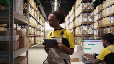 Afro-Amerikan kadın işçiler sipariş yönetimini sağlamak için barkod tarayıcılarını kullanıyorlar, tablet üzerindeki depodaki envanter sistemini güncelliyorlar. E-ticaret dağıtım merkezi. Kamera A.