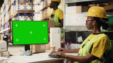 Afrika kökenli Amerikalı bir kadın polis memuru, depo ortamında çelik yelek ve miğfer takıyor. E-ticaret perakende operasyonları büyük kutularla çevrili. Kamera B.