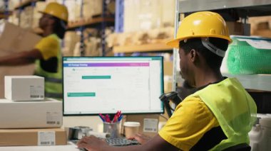 İthalat işlemi sırasında kara depo personeli kargo mallarını doğruladı. Yelek ve miğfer giyerken dağıtım merkezindeki düzgün takip numaralarını yönetiyordu. Kamera B.