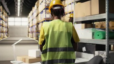 Lojistik merkezde çalışan Afrikalı Amerikalı bir kadın. Bilgisayarla ilgili bilgileri takip ediyor. Teslimat güzergahını ve diğer sevkiyat detaylarını gerçek zamanlı olarak güncelliyor. Çevrimiçi siparişler için paket durumunu takip ediyorum. Kamera A.