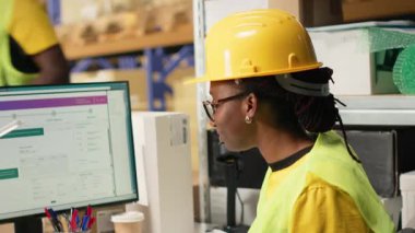 Afrika kökenli Amerikalı kadın UHB etiketlerinin sevkiyat detaylarını onaylıyor, paket izleme yazılımını kullanarak doğru sipariş statüsüne sahip. Depo 'daki ithalat işlemleri denetleniyor. Kamera B.