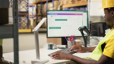 Siyah lojistik işçileri bilgisayar yazılımında kargo takibi yaparak kargo etiketli kutular için hızlı teslimat sağlıyorlar. Endüstriyel e-ticaret dağıtım operasyonları devrede. Kamera B.