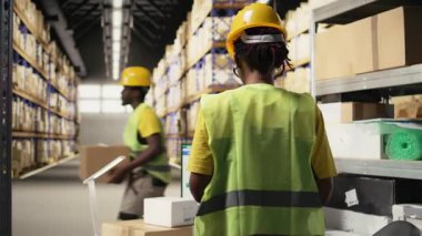 Afro-Amerikan depo memuru, takip bilgilerini bilgisayar yazılımında güncellemek için paket güzergahını denetliyor, tatbikat merkezinde yelek ve miğferle çalışıyor. Kamera A.