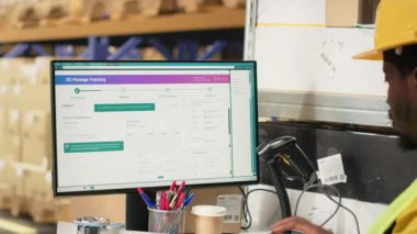 Afrikalı Amerikalı çalışanlar etiketleri tamir ediyor ve kutulardaki barkod etiketlerini tarıyor. Dağıtımdan önce malları ve sevkiyat detaylarını kaydediyor. İzleme bilgilerinde tarayıcı kullanılıyor. Kamera B.