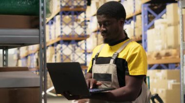 Depo görevlisi, büyük bir dağıtım merkezindeki rafların detaylarını inceliyor. Depoda güvenlik üniforması giyiyor. Malzeme zinciri yönetimi ve depolama odasına sevk. Kamera B.