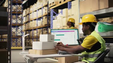 Afrikalı Amerikalı adam barkod işlemek ve endüstriyel depolama raflarındaki kutulara nakliye etiketleri yapıştırmak için tarayıcı kullanıyor. Paket izleme servisi için yapışkan etiketler taranıyor. Kamera A.