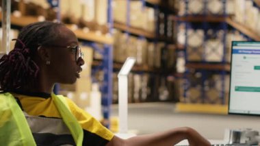 Kara depo ekibi gelen malların sevkiyatını denetliyor, kargo taşıma detayları için bilgisayardaki izleme yazılımını izliyor. Lojistik merkezinde yüksek yelekli iş arkadaşları. Kamera B.