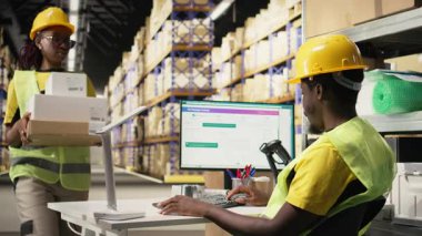 Siyah lojistik işçileri bilgisayar yazılımında kargo takibi yaparak kargo etiketli kutular için hızlı teslimat sağlıyorlar. Endüstriyel e-ticaret dağıtım operasyonları devrede. Kamera A.