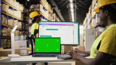 İthalat ihracat detaylarıyla ilgilenen erkek çalışan. Ekranda fotokopi alanı var. Depo masasında çelik yelek ve kask giyiyor. Personel izleme paketi yazılım takibi. Kamera A.