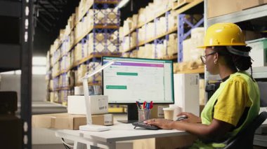 Barkodları ve sevkiyat detaylarını onaylayan siyah kadın etiketler ve izleme yazılımı, tedarik zinciri lojistiği ve e-ticaret dağıtımını yönetmeye odaklanıyor. İşçi envanteri gözden geçiriyor. Kamera A.