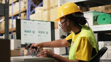 Yelekli siyah bir kadın tarayıcıyla takip bilgilerini kaydediyor, kargo siparişleri için ekspres teslimat servisini denetliyor. Etiketlerin sevkiyat detayları taranıyor, bilgisayar yazılımlarını takip ediliyor. Kamera B.