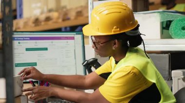 Barkodları uygulayan ve tarayan siyah işçiler kargo kutularındaki etiketleri yakalar, dağıtımdan önce malları ve sevkiyat detaylarını kaydeder. Depodaki takip numaralarında tarayıcı kullanılıyor. Kamera B.