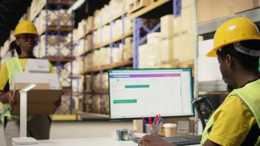 Afrikalı Amerikalı çalışanlar etiketleri tamir ediyor ve kutulardaki barkod etiketlerini tarıyor. Dağıtımdan önce malları ve sevkiyat detaylarını kaydediyor. İzleme bilgilerinde tarayıcı kullanılıyor. Kamera A.