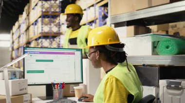 Afrika kökenli Amerikalı kadın UHB etiketlerinin sevkiyat detaylarını onaylıyor, paket izleme yazılımını kullanarak doğru sipariş statüsüne sahip. Depo 'daki ithalat işlemleri denetleniyor. Kamera A.