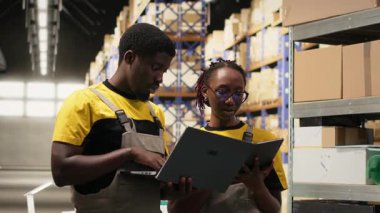 Siyahi iş arkadaşları büyük depoda sevkiyat için kutularda siparişler hazırlıyor, dizüstü bilgisayardaki envanterleri kontrol ediyor ve kargo dağıtımını yönetiyorlar. Lojistik yönetimi için paket tasnif ediyorum. Kamera B.