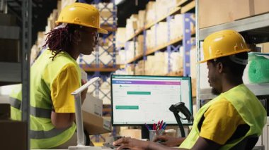 Depo operasyon ekibi gelen malları yönetiyor, kargo taşıma detayları için bilgisayardaki izleme yazılımlarını takip ediyor. Dağıtım merkezinde yeleği olan çalışanlar. Kamera B.