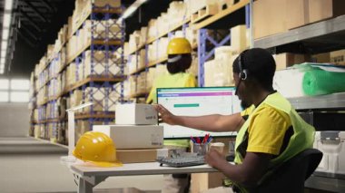 Siyah çağrı merkezi operatörü sipariş karışıklığı olan bir müşteriye yardım ediyor. Depo tesisindeki paket izleme yazılımının paket durumunu doğruluyor. Müşteri hizmetleri destek birimi. Kamera A.