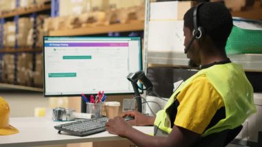 Siyah çağrı merkezi operatörü sipariş karışıklığı olan bir müşteriye yardım ediyor. Depo tesisindeki paket izleme yazılımının paket durumunu doğruluyor. Müşteri hizmetleri destek birimi. Kamera B.