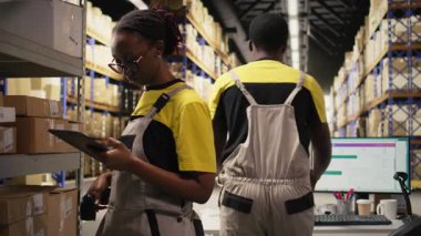 Siyah kadın çalışanlar, depodaki kutulardaki nakliye etiketlerini incelemek için barkod tarayıcısı kullanıyorlar. İz sürme bilgisi ve doğru lojistik ile paket izleme servisi için yanlış etiketler taranıyor. Kamera A.