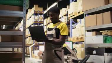 Genç zenci çalışanlar büyük bir depo tesisinde raflarda paketleri ayırıyorlar. Envanteri paketlenmiş malların etrafındaki bilgisayar ile yönetiyorum ve yerine getirmek için dağıtıma hazırım. Kamera A.