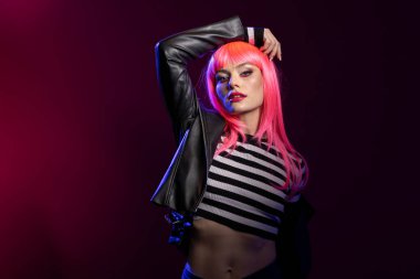 Dişi manken, deri ceketin içindeki gücü yoğun bir yüz ifadesiyle stüdyoda duruyor. Cesur bir kadın kendinden emin bir duruş içinde vahşi enerji ile poz veriyor, gözleri kamerayla kilitli..