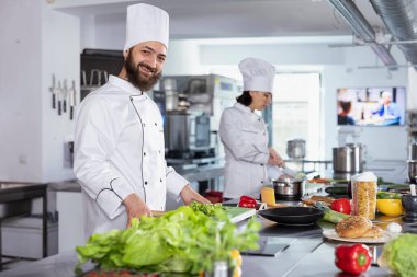 Bir restoranın mutfağında aşçılık uzmanı taze malzemelerle yemek hazırlıyor, modern mutfak aletleri ve meslektaşlarıyla tezgahlarda çalışıyor. Gurme meslek ve kariyer.