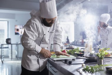 Aşçı mutfak tezgahında sarımsaklı karanfillere bıçak dayayıp ezilmiş baharatları ve tatları kesme tahtasına döküyor. Genç aşçı lezzetli malzemelerle yemek yapıyor..