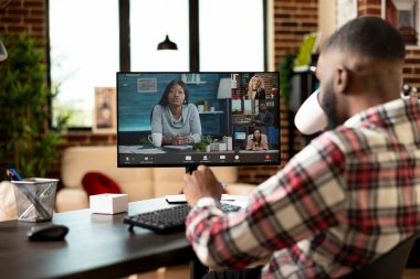 Uzaktan kumandalı siyah işçi, sanal toplantı sırasında kahve içiyor ve çeşitli meslektaşlarını dinliyor. Çevrimiçi beyin fırtınası oturumunda, stratejik iş fikirlerini paylaşan Afrikalı Amerikalı girişimci