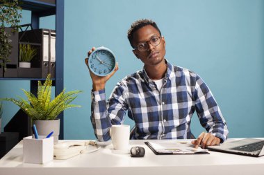 Masasında bir pano ile oturan ve elinde çalar saat tutan Afro-Amerikan serbest çalışanın portresi. Evrak işleriyle ilgilenen genç bir iş analisti ve elinde analog bir saat sunuyor..