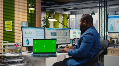 Siyah analist dizüstü bilgisayardaki kroma tuşlu grafikleri analiz etmek, iş yönetimi verimliliğini artırmak ve kalkınma hedeflerine ulaşmak için strateji raporları hazırlamak için bilgisayar kullanıyor.