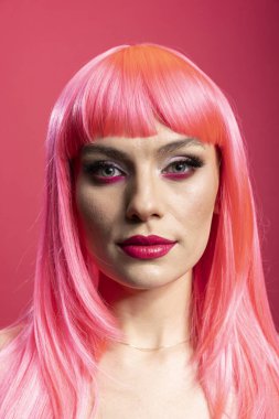 Şık bir model, sakin bir görünüm, kendine güvenen bir görünüm, yontulmuş yüz hatları ve şık bir saç stili. Kalın makyajlı ve saçlı, pembe arka planda objektife bakan güzel bir kadın.