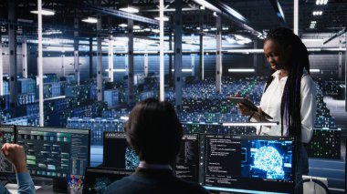 Veri merkezi geliştiricilerinden oluşan bir ekip beyin fırtınası yapıyor, sinir ağı AI LLM 'yi izliyor. Yüksek teknoloji tesisinde çalışan takım arkadaşları sunuculara güç veren makine öğrenme süreçlerini denetliyor, kamera A