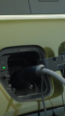 Yükleme rıhtımına bağlı EV aracının dikey videosu sürdürülebilirliği vurguluyor. Elektrik şebekesine bağlı elektrikli arabanın görüntüsü, küresel çevre dostu itmenin bir parçası.