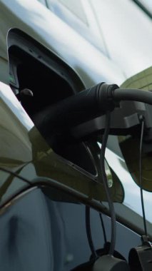 Sürücünün EV aracını yükleme limanından ayırdığı dikey video, düşük karbon ayak izi taahhüdü kavramı. Elektrikli arabanın fişini çeken adam şarj üstüne şarj, düşük açılı çekim.