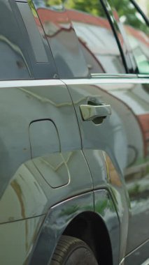 Dikey video sürücüsü işe giderken elektrikli cipi şarja takıp sera gazı emisyonunu azaltıyor. İstasyonda şarj edilmek üzere yeşil EV aracını park eden adam.