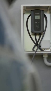 Duvar monte edilmiş EV araba şarj istasyonunun dikey videosu şarj için hazır, düşük karbon ayak izi taahhüdü kavramı. Güvenli ev kullanımı için koruyucu dış kaplamada EV şarj ünitesi