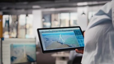 Temiz enerji üretimi için tasarlanmış fütüristik rüzgar türbini üzerinde çalışmak için tablet kullanan teknisyenleri kapatın. İşçi dokunmatik ekran aygıtında geçiş yapıyor, son teknoloji VAWT yenilikleri tasarlıyor, kamera A