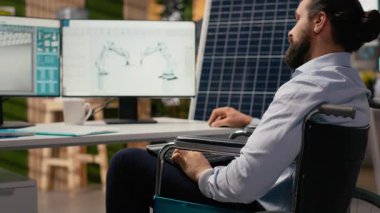 Tekerlekli sandalyedeki engelli Ar-Ge araştırmacısı güneş enerjisi sistemleri okuyor. Belden aşağısı felçli çalışanlar fotovoltaik karbon ayak izini geliştirmek için çalışıyorlar, kamera B
