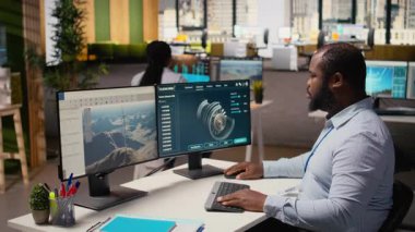 Ofiste rüzgar türbini simülasyonu üzerinde çalışan bir teknisyen güncelleme yapıyor. Ar-Ge bölümündeki Afrikalı Amerikalı adam bilgisayarda CAD yazılımı kullanıyor, yenilenebilir enerji yel değirmeni mühendisliği yapıyor, kamera A