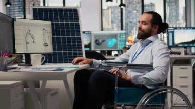 ArGe ofisinde belden aşağısı felçli bir adam yeşil teknoloji güneş panelleri tasarlıyor. Tekerlekli sandalyedeki engelli çalışanlar güneş pillerini, temiz enerji üretimini ve kamera B 'yi geliştirmek için simülasyon çalıştırıyorlar.