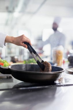 Kadın aşçı fırında gurme yemeği için lezzetli bir biftek hazırlıyor. Çiğ eti tavada maşayla çeviriyor. Mutfak uzmanı yağ ve gastronomi filetosu hazırlıyor. Kapat..