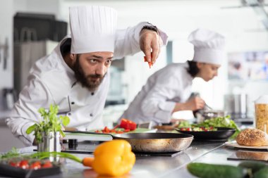 Üniforma konusunda gastronomi uzmanı taze sebzeli bir gurme yemeği için kesilmiş dolmalık biber ekliyor, profesyonel bir restoranda çiğ sebzelerle lezzetli bir yemek tarifi oluşturuyor..