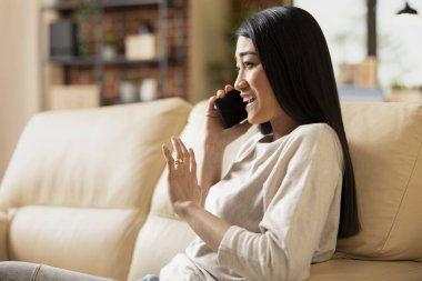 Gülümseyen iş kadını yatırımcıyla mobil cihazda konuşuyor, verimli sohbetin tadını çıkarıyor. Kanepede oturan neşeli bir kadın serbest yazar. Telefondan kulağa, potansiyel müşteriyle konuşuyor..