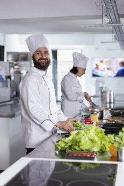 Modern bir mutfakta, mutfak aletleri ve paslanmaz çelik kaplar kullanarak taze ürünlerle dolu gurme yemekleri hazırlayan profesyonel bir aşçı. Gastronomi sektöründe çalışan bir erkek aşçı..