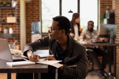 Şirket büyüme stratejilerini araştıran, profesyonel bir çevrede çeşitliliği ön plana çıkaran engelli bir çalışan. Tekerlekli sandalyedeki adam laptoptaki verileri incelerken rapor yazıyor..
