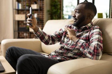 Uzaktan kumandalı erkek yönetici kanepede oturur, cep telefonuyla sanal takım toplantısı düzenler. Video görüşmesinde profesyonel mali danışman, başlangıç stratejilerini tartışıyor ve iş iletişimini yönetiyor.