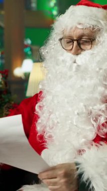 Noel Baba kılığındaki dikey videocu çocuklardan gelen mektupları okurken neşeli tavırlar sergiliyor. Kırmızı Noel Baba kostümü giyen kişi çocukların Noel dileklerini okumak için neşeli bir ortam yarattı.