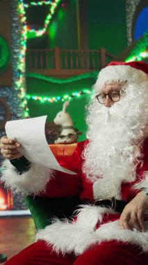 Dikey video Noel Baba 'nın süslemelerle çevrili çocuklardan gelen mektupları okurken sandalyede uyumasından yoruldu. Yorgun yaşlı bir adam, çocuklara Noel dilek listesi ve kamera okurken uykuya dalar.